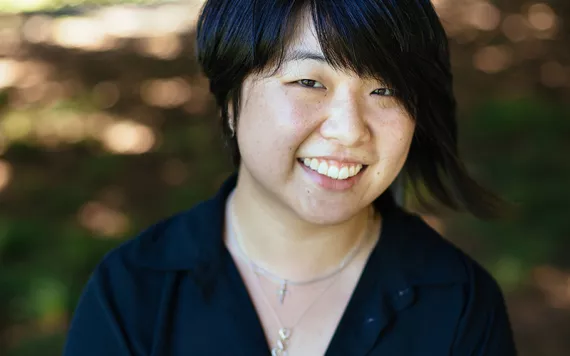 Marci Calabretta Cancio-Bello smiles at the camera. Cancio-Bello has short, dark cropped hair and is wearing a black long-sleeved shirt.