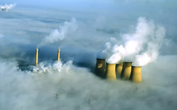 Yellowish gray smokestacks emerging from a rolling white blanket of fog