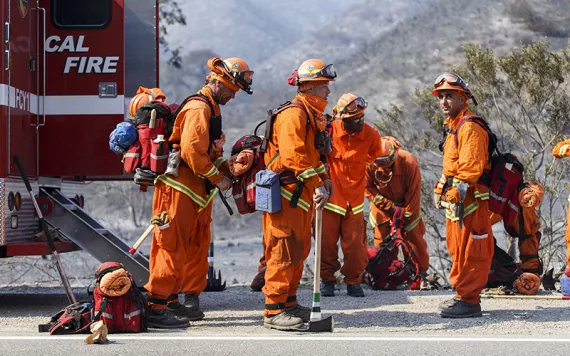 Firefighters in orange firefighting suits in front. of a hazy California landscape