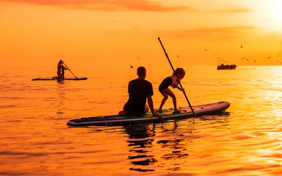 Paddleboarders silhouetted against an orange sea and sky