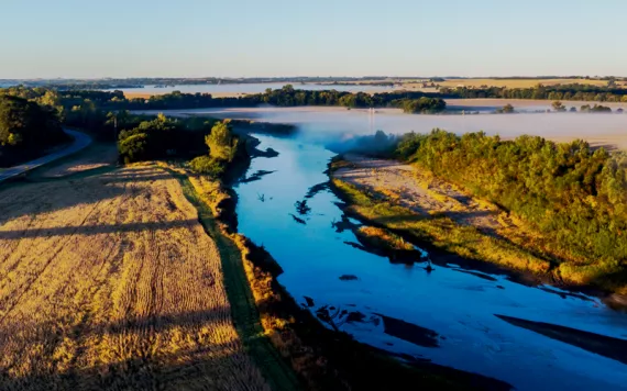 Aerial view of the West Nodaway River with agricultural fields surrounding it and blue skies above.