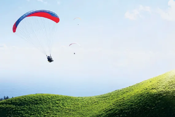 Three paragliders descend along the curvy flanks of Mt. Tamalpais in Marin County, California, overlooking the Pacific Ocean. 