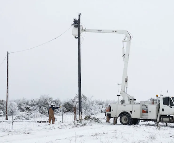 Linemen repair a utility line in a field covered with snow.