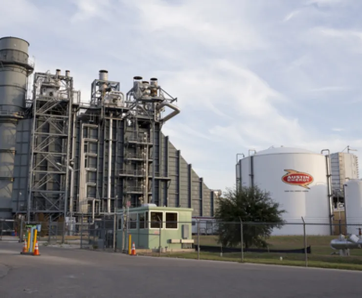 A fracked gas power plant and Austin Energy gas container surrounded by blue sky and clouds.