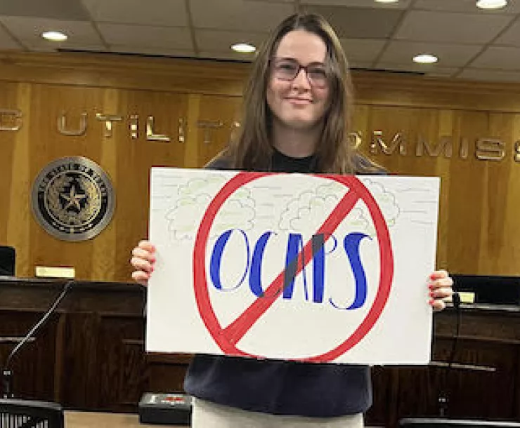 Woman stands in agency meeting room with sign that says No to OCAPS