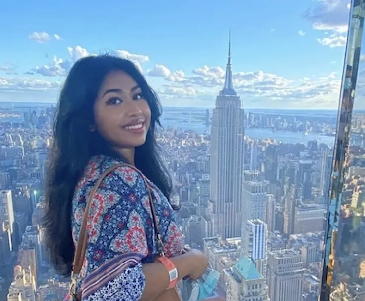 Woman smiles by window looking out at New York City skyline. 