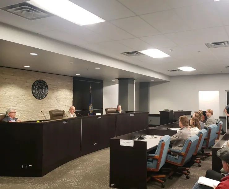 Picture of PUC hearing room, PUC seal on back wall, people sitting in chairs facing Commissioners