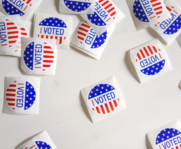 Many "I voted" stickers with red, white, and blue scattered over a white table top.