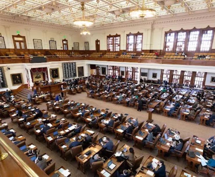 A view of policymakers sitting at desks on the floor of the Texas House of Representatives as seen from the balcony.