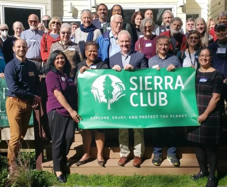 A group of volunteers and elected officials gather in front of Sierra Club sign outside 