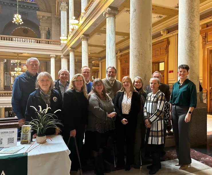 A group of 12 people standing for a photograph at the Indiana Statehouse. To the left, half of a table is in the photo which shows the Sierra Club logo.