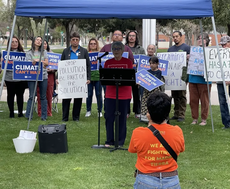 Group of people standing behind a person speaking with 'Clean Air Now" & climate signs 