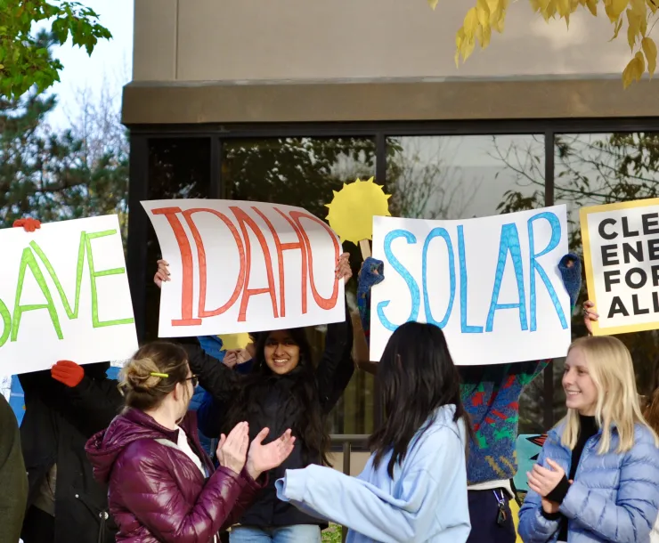 PIcture of young people holding up signs that say "Save Idaho Solar" and "Clean Energy for All" at a rally