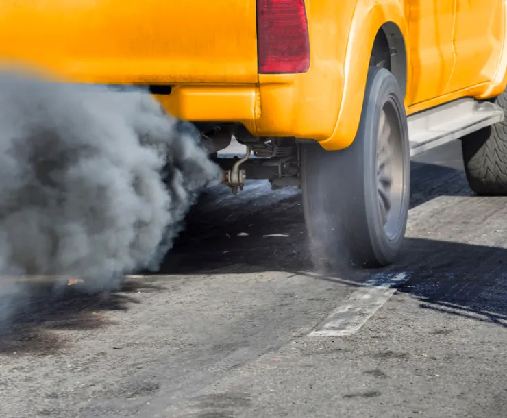 An orange pickup truck spews dark, gray exhaust.
