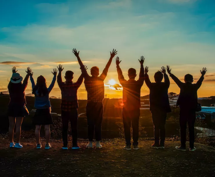 youths with arms reaching toward sky as sun sets
