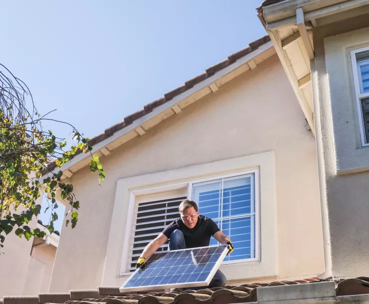 man holding solar panel on house roof