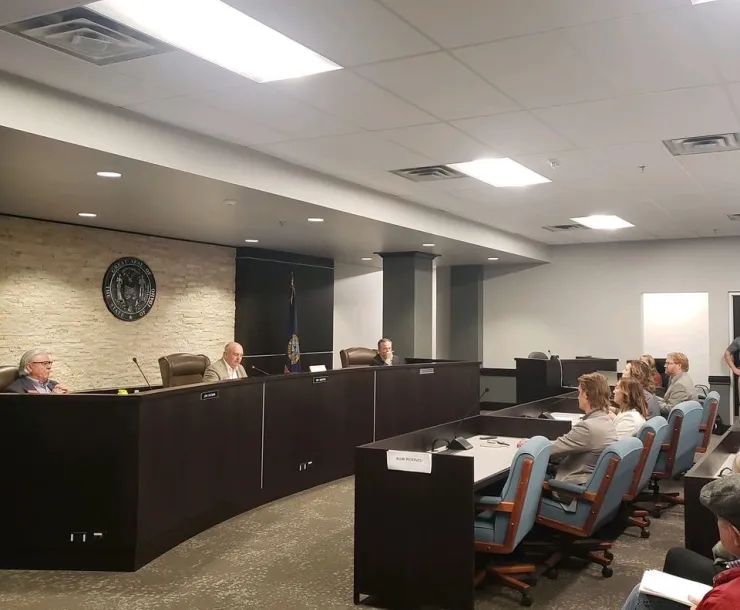 Picture of PUC hearing room, PUC seal on back wall, people sitting in chairs facing Commissioners