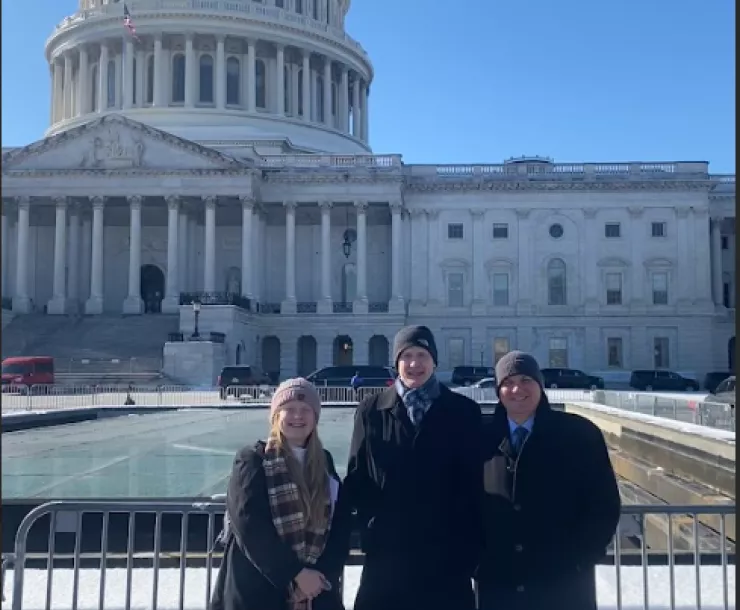 Three people standing outside the Capital building in DC. It's a bright cold day. 