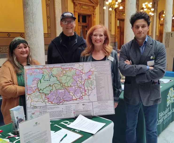 Four people stand at a table at the Indiana Statehouse. They are standing around a map.