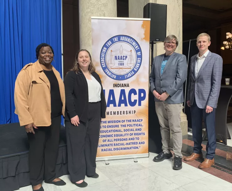 Four people stand at an indoor venue, smiling for the camera. They are standing by an NAACP banner.