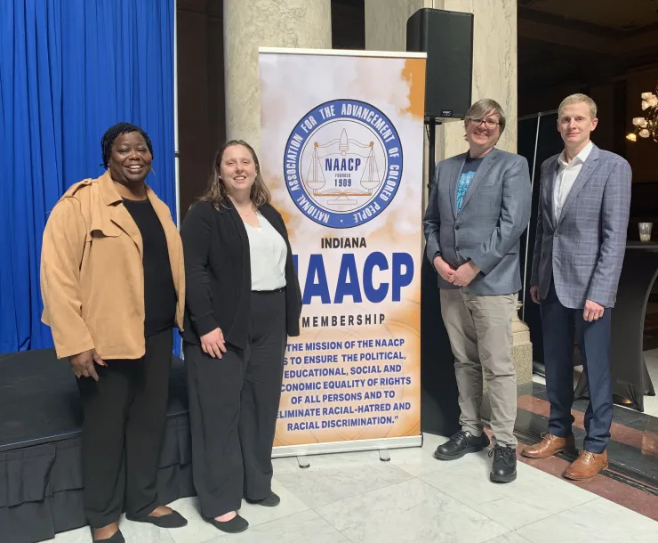 Four people stand at an indoor venue, smiling for the camera. They are standing by an NAACP banner.