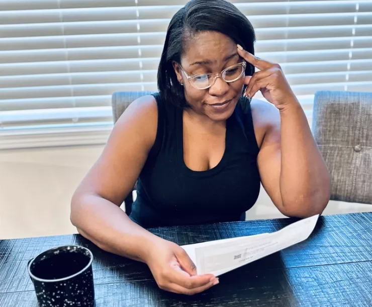 Woman, sitting at a kitchen table, looking at a energy bill with an expression of exasperation.