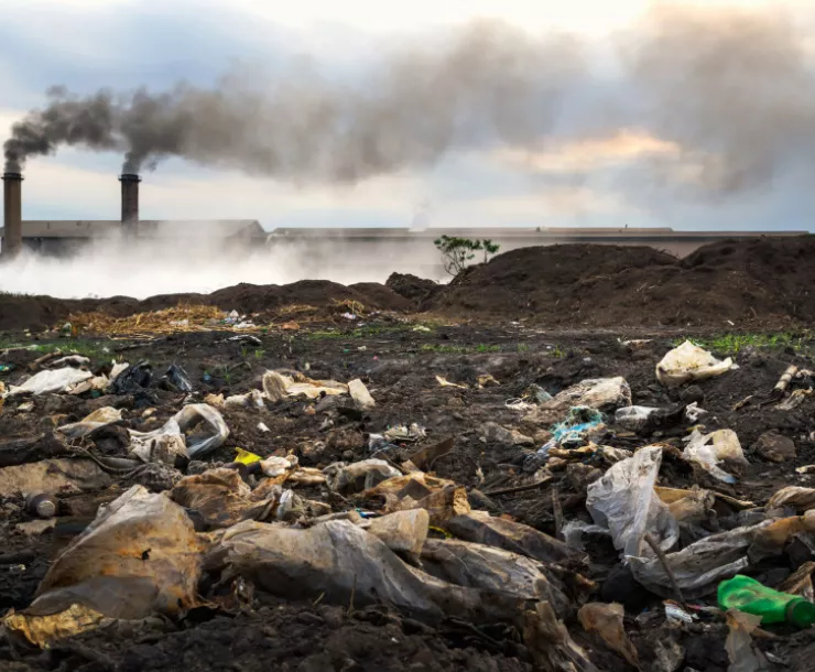 Plastic pollution on the ground with smoke stacks in the background emitting dirty air