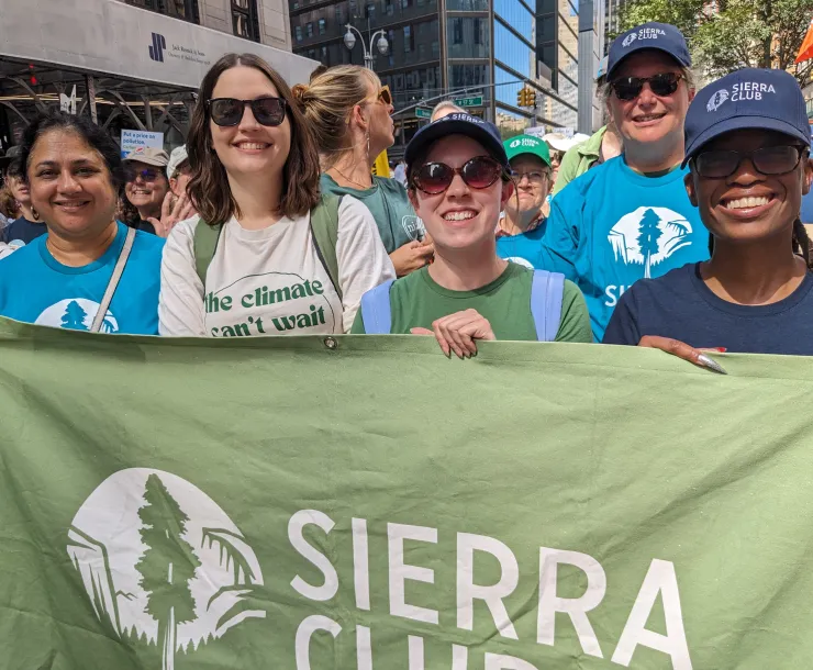 A diverse group of Sierra Club staff and volunteers hold a large green banner with Sierra Club's logo at the March to End Fossil Fuels.