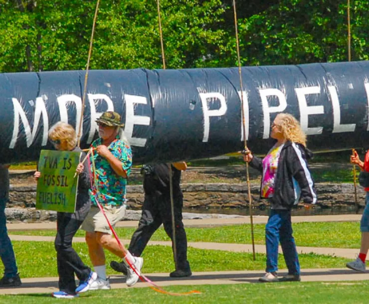 environmentalists demonstrate at event in Nashville, holding huge pipeline that reads "No More Pipelines"