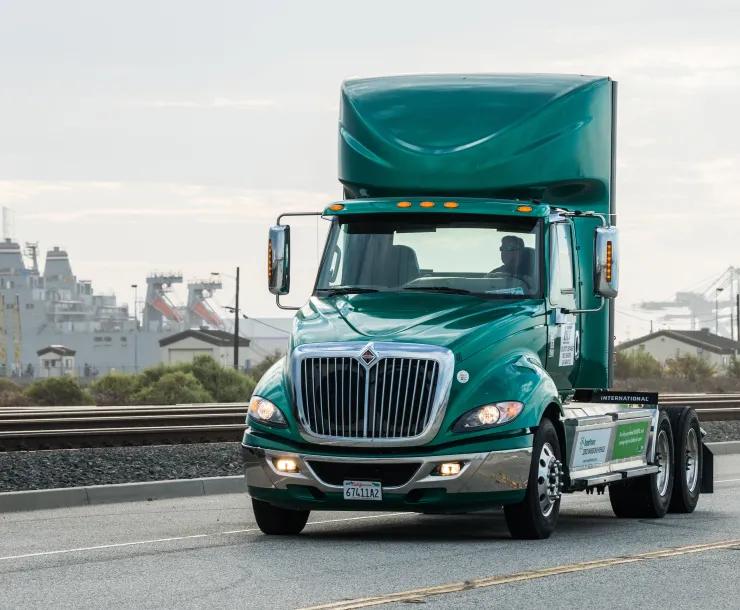 Green Heavy Duty Electric Vehicle driving across highway. 