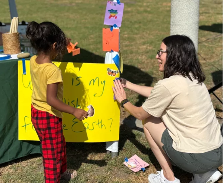 Woman squatting down, talking with a small child in front of a hand-made poster