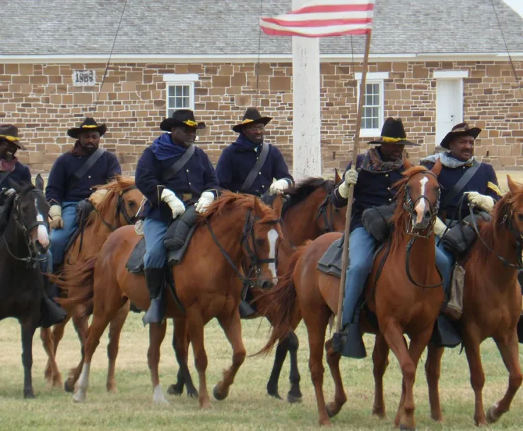 Black men dressed as soldiers on horses in front of stone building