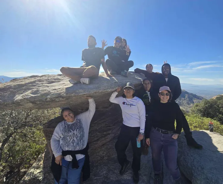 a group posing next to and on a large boulder