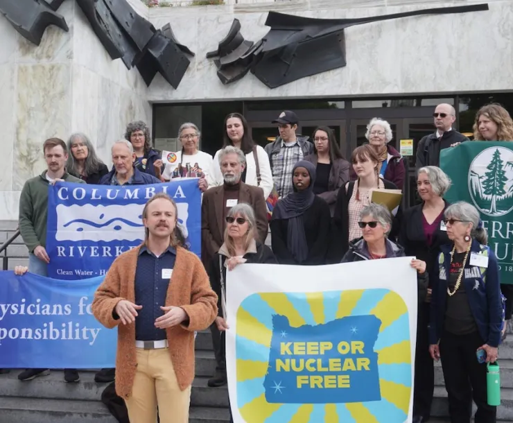 A group of people holding various signs stands on a large stone staircase in front of the Oregon capitol building.