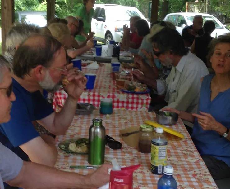 People sitting along a picnic table talking and eating food.