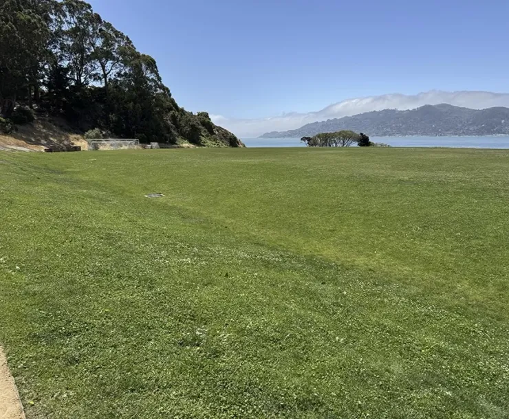 Wide expanse of bermuda grass sports field, water and hills in background