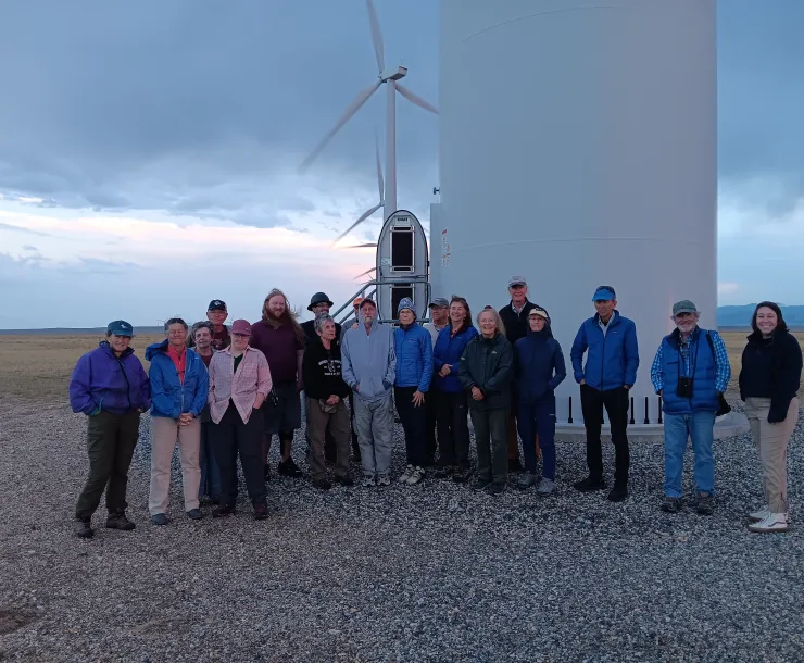 A group of people pose in front of a wind turbine.