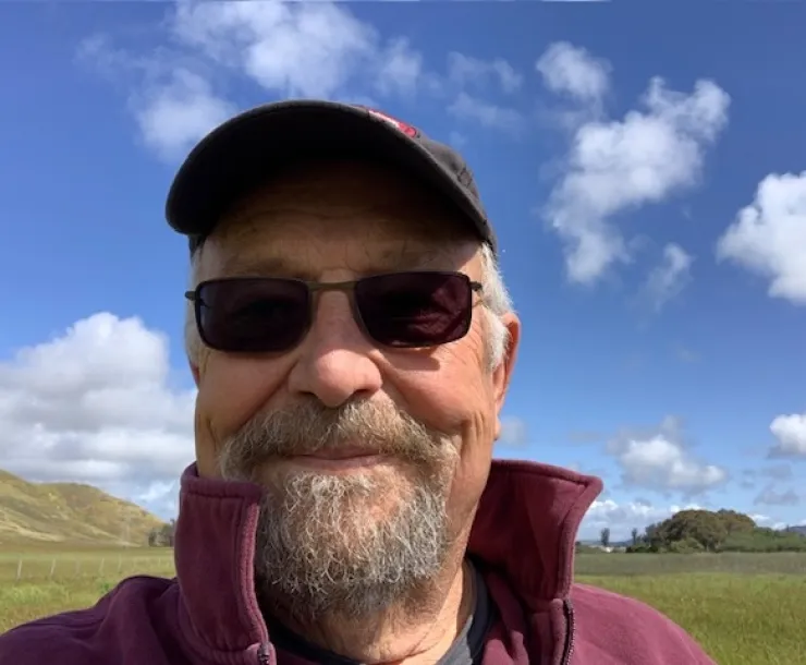Chapter Outings chair Art Westerfield, wearing a hat and sunglasses standing in front of green hills.