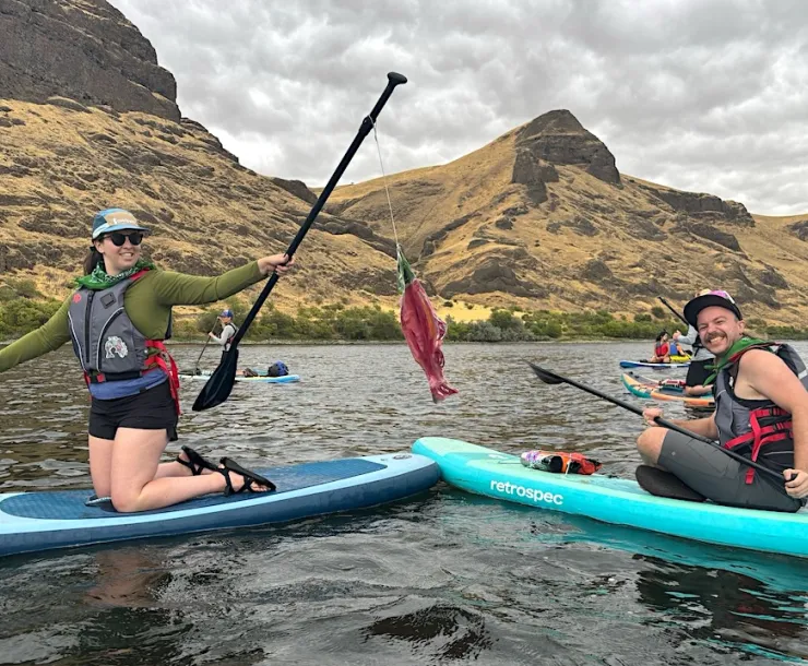 Two people sit on paddle boards on a river