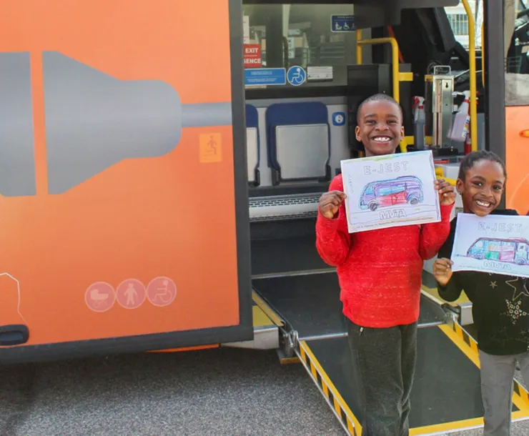 Two kids pose with drawings in front of MVTA's electric mini-bus