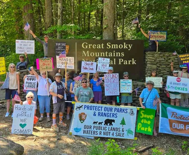 group of people hold signs in front of Great Smoky Mountains national park entrance sign