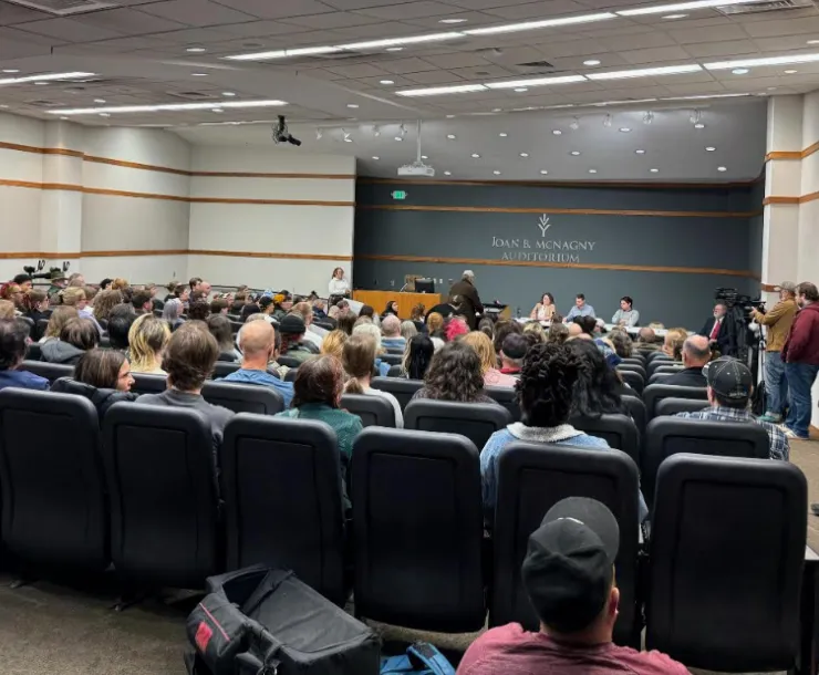 A packed room of folks sitting and standing at a public hearing