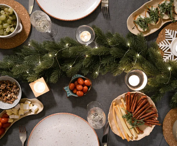 A table is laid out with several dishes of food around an evergreen garland and some small white candles.