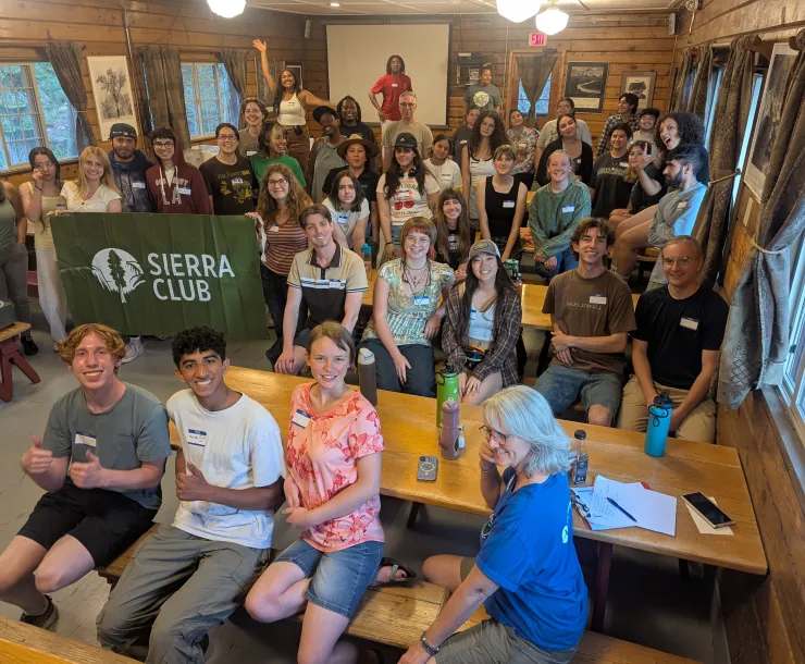 Picture of lots of young adults sitting in a log cabin space with a big Sierra Club banner