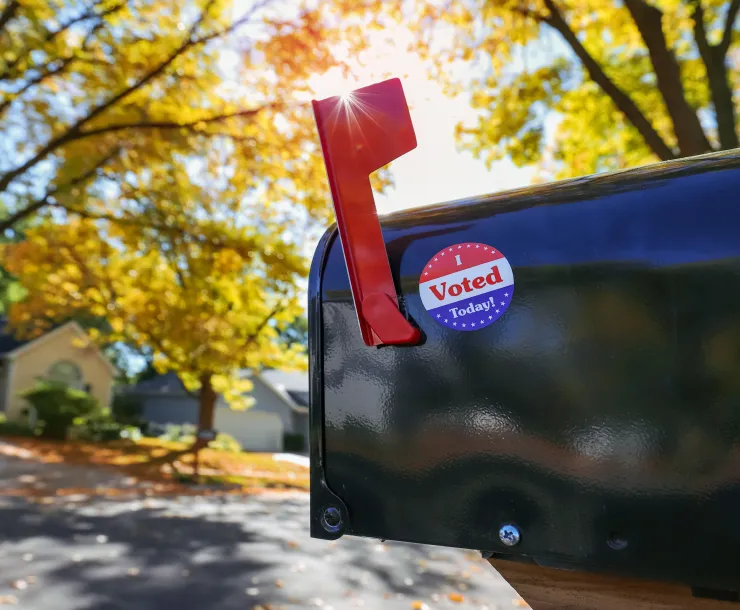 Mailbox with an "I voted today" sticker on it with sun flare behind flag, absentee voting through the mail