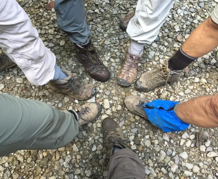 A photo showing the lower legs and hiking boots of seven different people. They've all put one foot forward to have their feet in a circle.