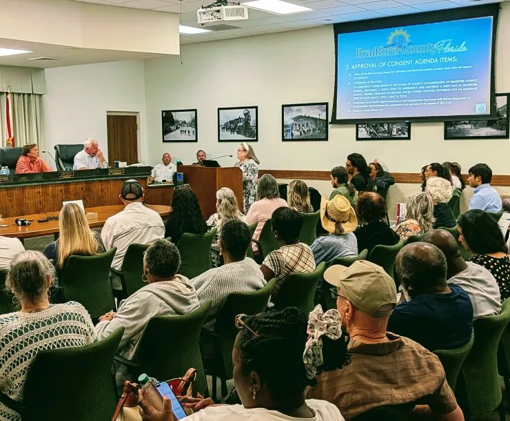Bradford County Commissioners listening as resident speaks at the podium in a roomful of local residents listen while seated