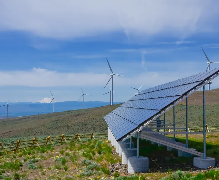 a shrub steppe grassland under blue skies with a solar panel in the foreground and several wind turbines in the background