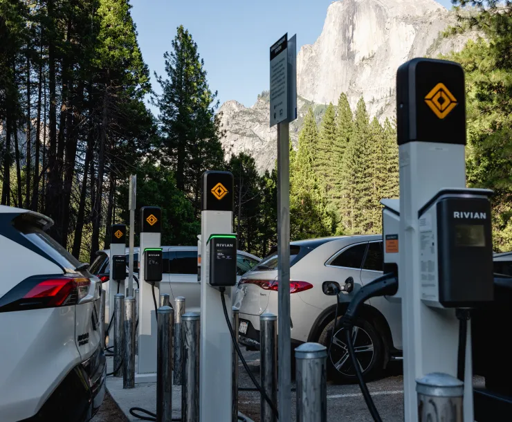 a row of electric vehicle chargers and cars with Yosemite National Park in the background