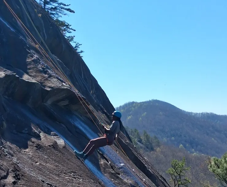 A person rappels down a sloped cliff during a spring 2026 outing in NC led by Lindsey Hildebrand